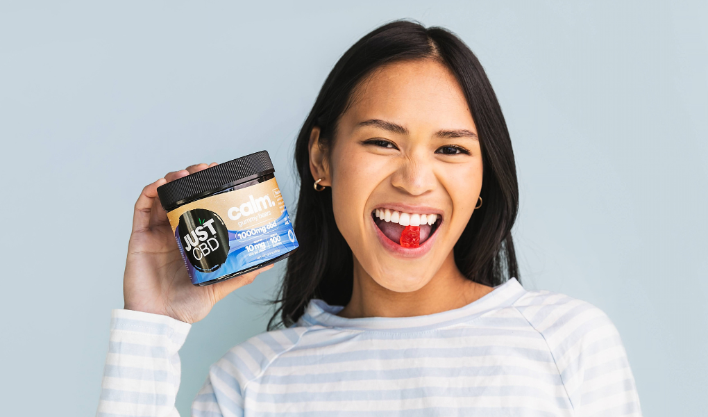 A women in a blue background holding a CBD gummy jar in her right hand