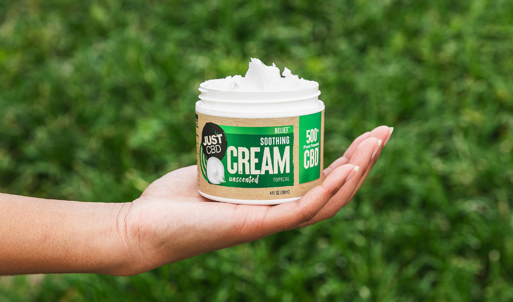 Hand holding a jar of 'Just CBD' cream against a grassy background