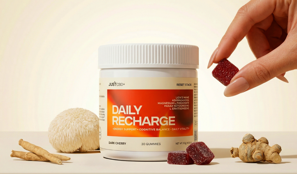 JustFood Daily Recharge gummy supplement container with a hand holding a gummy and natural ingredients on a light background
